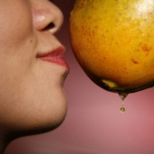 profile of a woman with a mango near her face smiling and smelling the mango